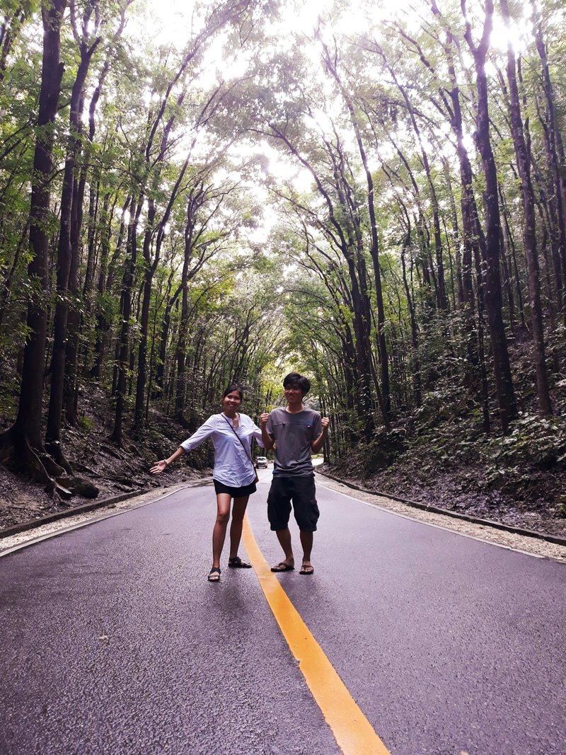 a young couple in the middle of the road that passes through a forest