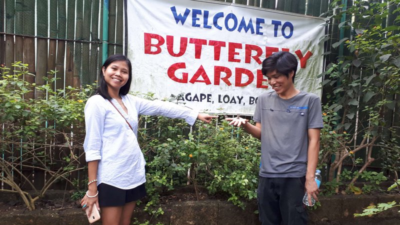 young couple with a banner that says 'Welcome to Butterfly Garden' behind them