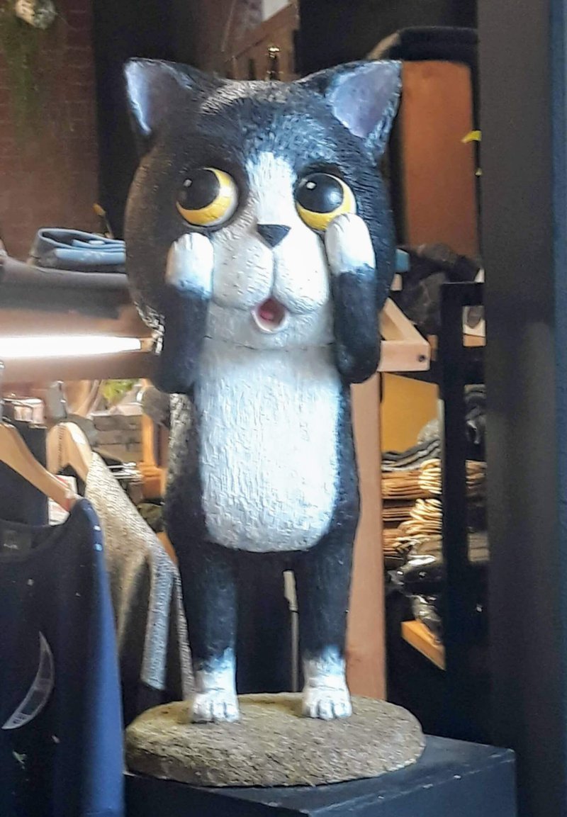 A cat statue, black and white, with yellow eyes. Paws are up on its face, as if in shock or disbelief.